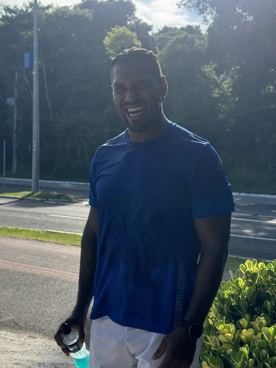 Christian Soares sorrindo ao ar livre depois do treino, com uma garrafa de isotônico na mão